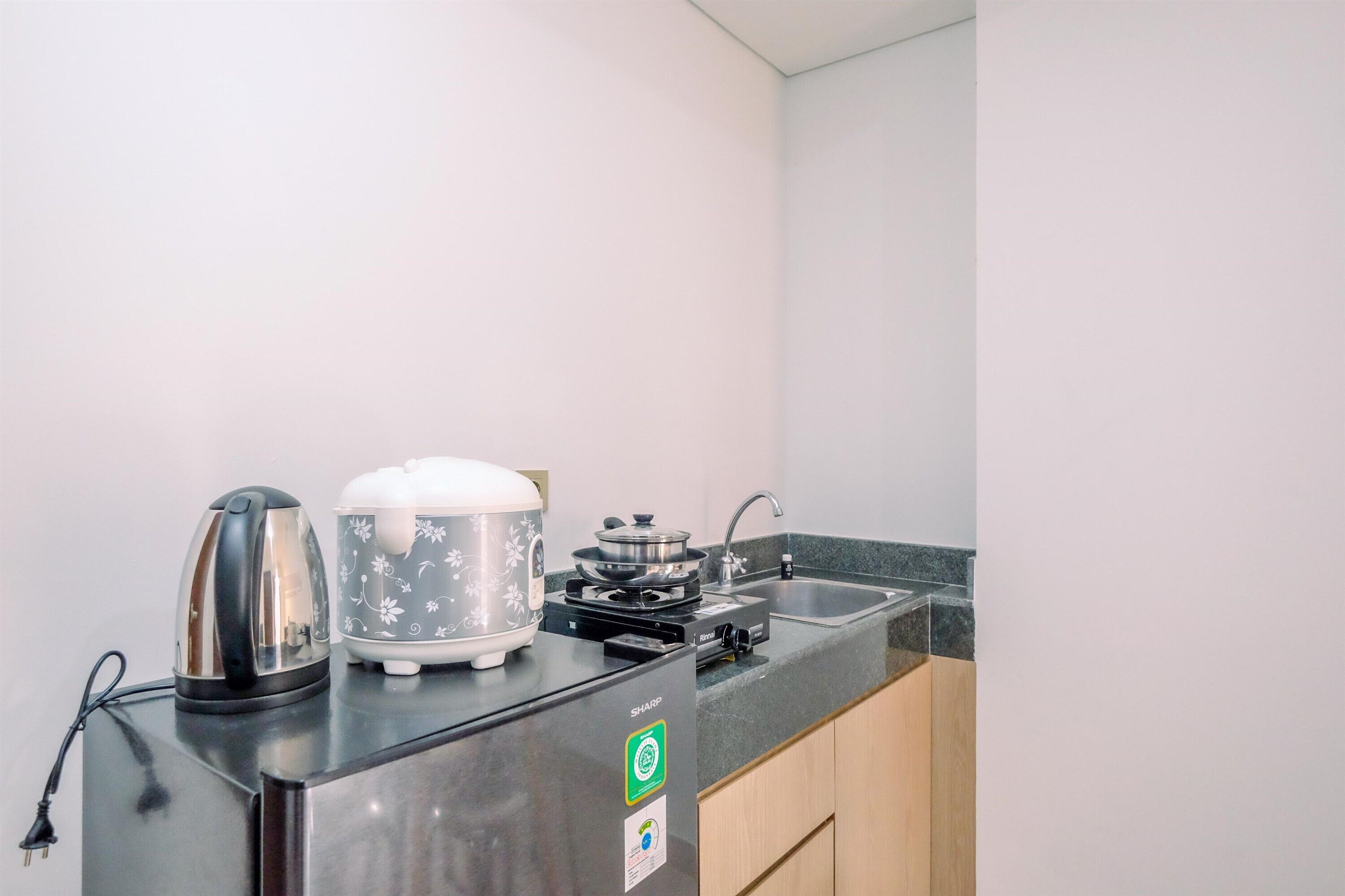 A compact kitchen with a stainless steel refrigerator, a kettle, a rice cooker, and a gas stove.