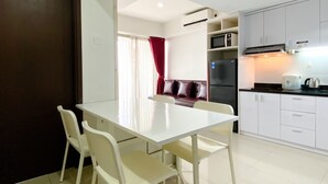 A compact kitchen with white cabinets, a microwave, a refrigerator, and a dining area with a white table and chairs.