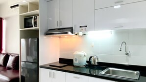 A modern kitchen with white cabinets, a stainless steel refrigerator, a kettle, and a sink.