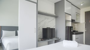 A modern hotel room with a bed, a TV, a small desk, and a kitchenette.