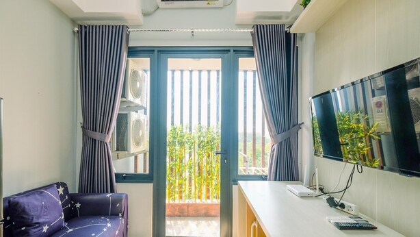 Ein Zimmer mit einer Couch, einem Schreibtisch mit Computer und Bildschirm sowie einer Glasschiebetür, die auf einen Balkon mit Pflanzen führt.