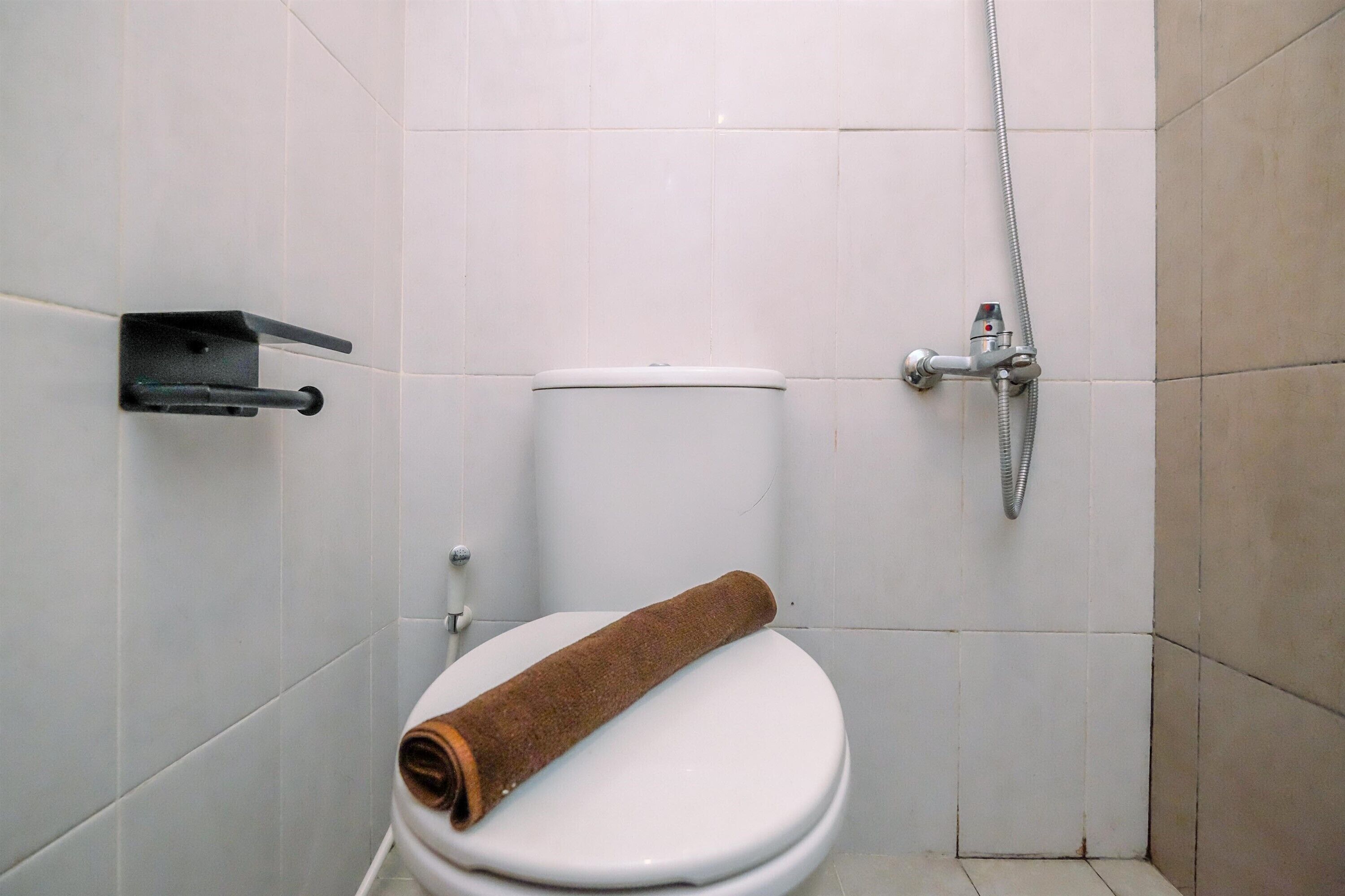 Un baño con inodoro blanco, una toalla en el asiento, cabezal de ducha y toallero.