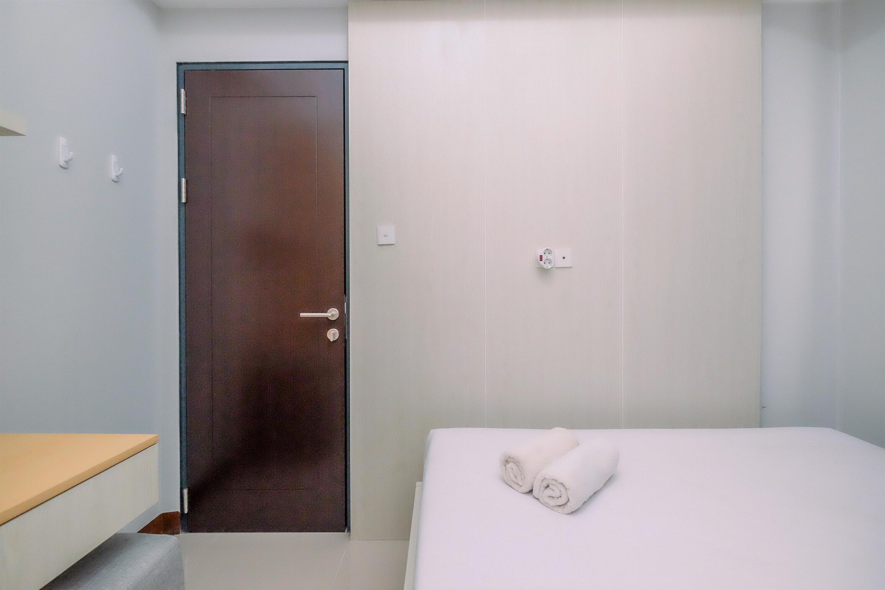 A hotel room with a wooden door, a bed with white bedding, and a small bedside table.
