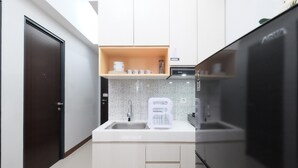 Eine kompakte Küche mit einem Kühlschrank, einer Spüle und einer Mikrowelle. Über der Spüle befindet sich ein Regal mit Geschirr und einem Wasserkocher.
