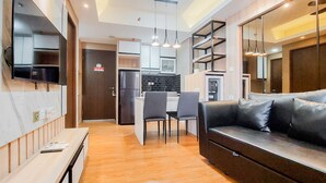 Un salon moderne avec un canapé, un coin repas avec des chaises, une cuisine équipée d’un réfrigérateur et un téléviseur fixé au mur.
