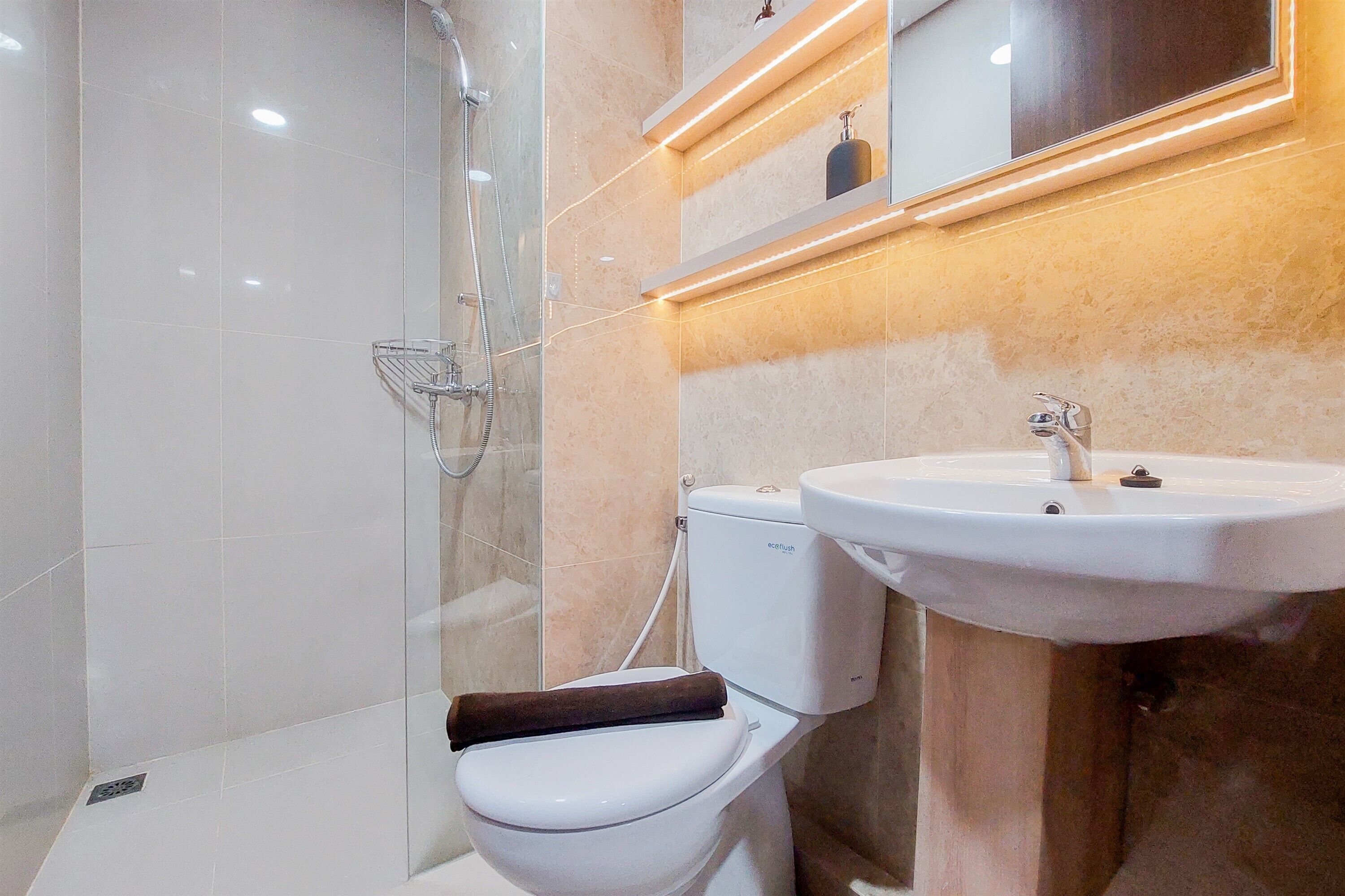 Un baño moderno con ducha envuelta en vidrio, inodoro blanco y lavamanos con espejo superior.