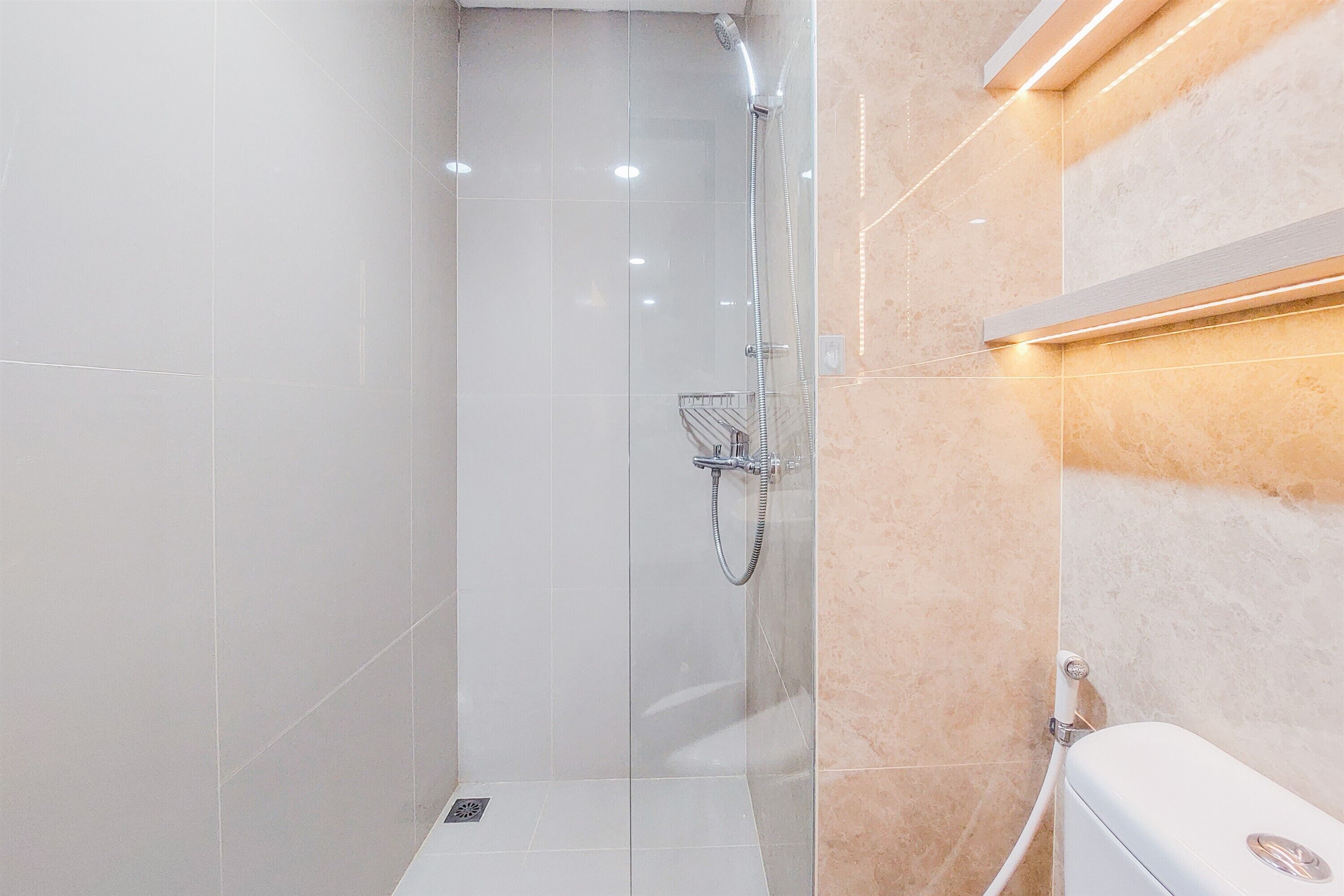 Une salle de bain moderne avec une douche à parois de verre, des toilettes blanches et un mur recouvert de carreaux beiges.