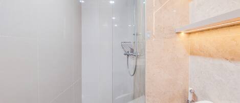 Une salle de bain moderne avec une douche à parois de verre, des toilettes blanches et un mur recouvert de carreaux beiges.