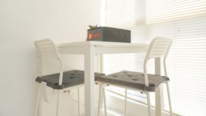 A small, white table with two white chairs, a black box with a logo, and a window with blinds. - Best Choice And Homey Studio Tifolia Apartment (Jakarta)