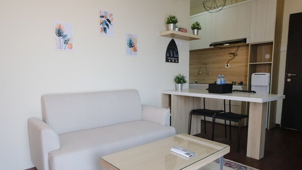 A modern living room with a sofa, a glass-top coffee table, and a kitchen area with a countertop, chairs, and a sink. - Spacious 2Br At Grand Asia Afrika Apartment (Bandung)