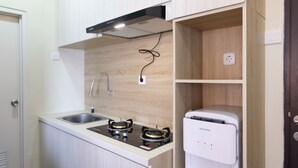 A compact kitchen with a gas stove, a built-in sink, and a white refrigerator. - Spacious 2Br At Grand Asia Afrika Apartment (Bandung)