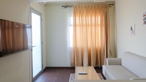 A room with a sofa, a coffee table, a TV, and a window with curtains. - Spacious 2Br At Grand Asia Afrika Apartment (Bandung)