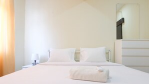 A hotel room with a bed, a nightstand, a lamp, a mirror, and a towel on the bed. - Spacious 2Br At Grand Asia Afrika Apartment (Bandung)