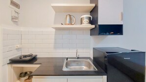 A kitchen with a black countertop, stainless steel sink, white cabinets, and a black refrigerator. - Scenic And Homey Studio Barsa City Apartment (Yogyakarta)