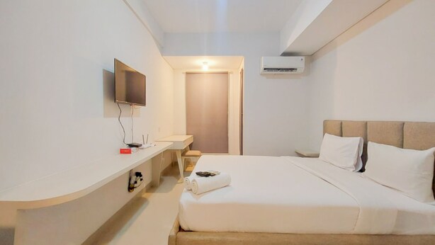 A hotel room with a bed, a TV mounted on the wall, a bedside table, and an air conditioning unit. - Scenic And Homey Studio Barsa City Apartment (Yogyakarta)