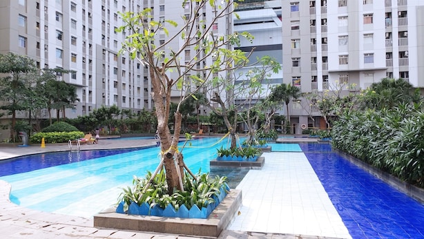 A swimming pool area with multiple lanes, surrounded by trees and plants, and adjacent to a high-rise building. - Stunning And Homey 2Br Green Bay Pluit Apartment (Jakarta)