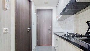 A narrow kitchen with a dark wooden door, a gas stove, and white tiled walls. - Best Homey And Nice Studio At Bintaro Icon Apartment (South Tangerang)