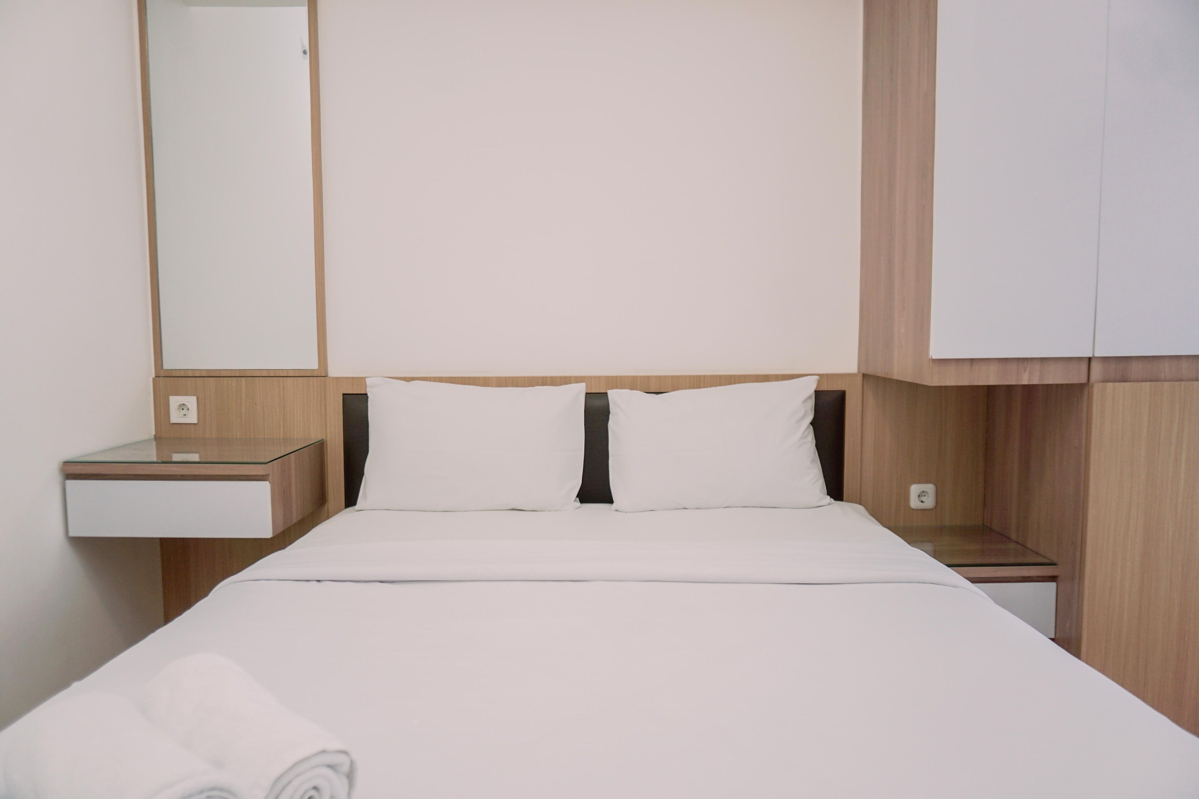 A neatly made bed with white linens, a wooden headboard, and a nightstand with a lamp.