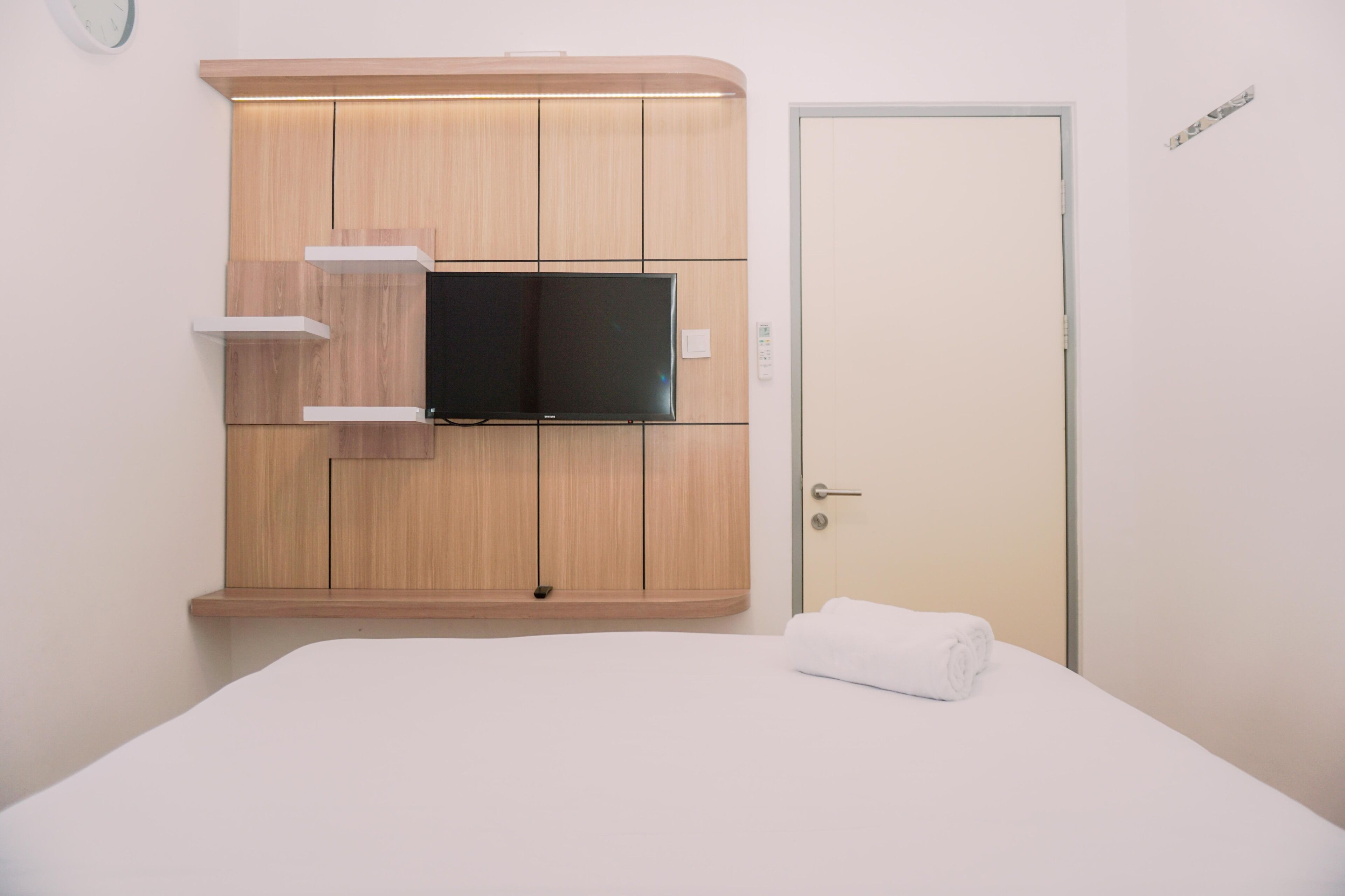 A hotel room with a bed, a TV mounted on a wooden cabinet, and a door.