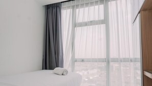 A hotel room with a bed, a window with sheer curtains, and a view of the cityscape. - Modern Look 2Br Apartment M-Town Residence (Gading Serpong)