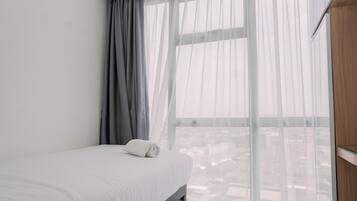 A hotel room with a bed, a window with sheer curtains, and a view of the cityscape.