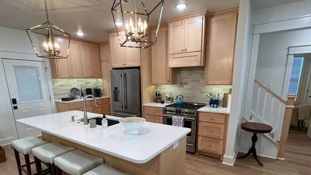 A modern kitchen with a central island, wooden cabinets, stainless steel appliances, and a pendant light fixture.