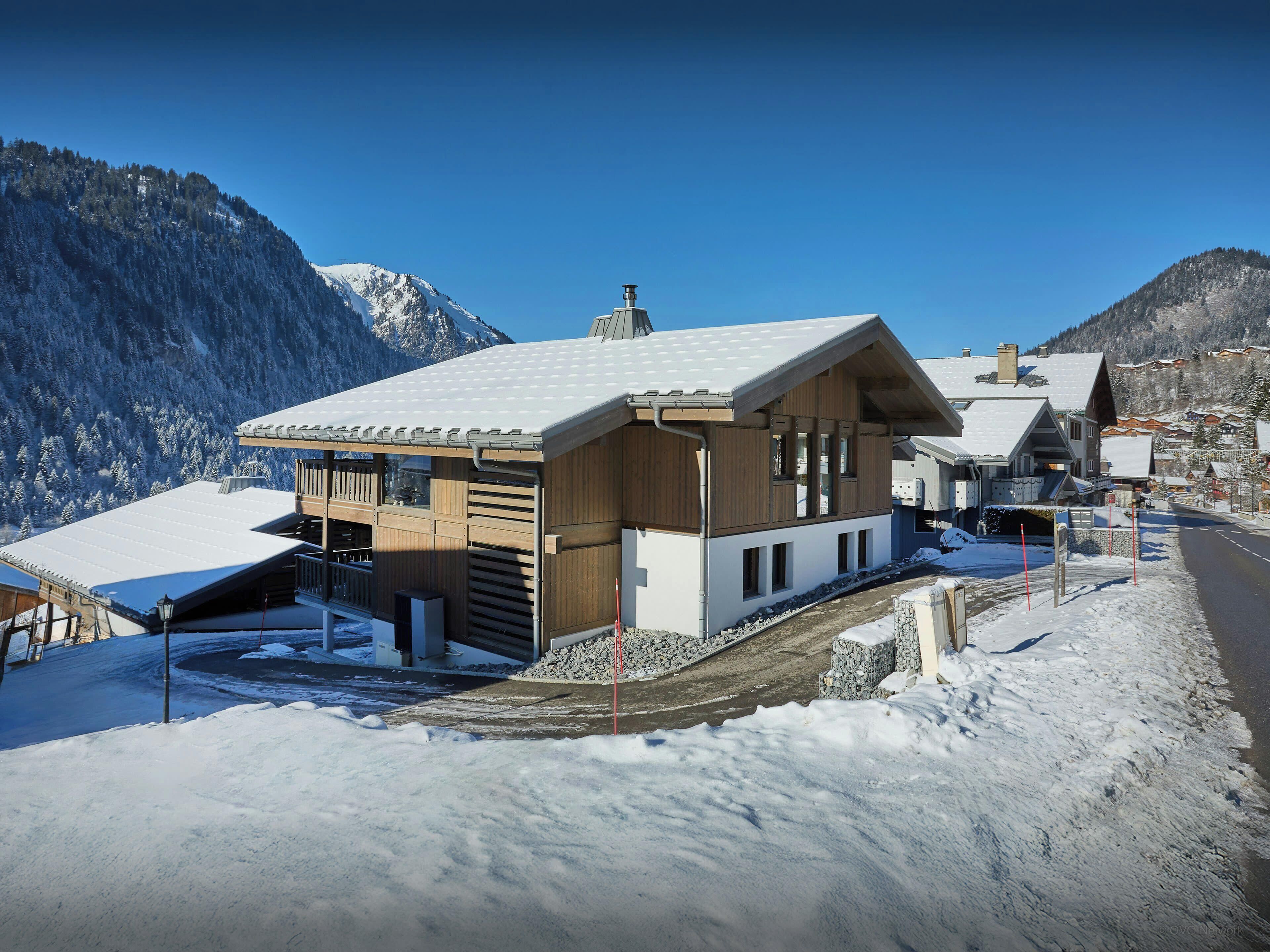 A modern chalet with a sloped roof, wooden exterior, and a snow-covered landscape.