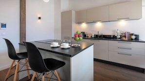 Een moderne keuken met een centraal eiland, zwarte stoelen en een koffieapparaat.
