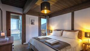 Een slaapkamer met een houten plafond, een groot bed met witte lakens, twee bedlampen en uitzicht op de omgeving.