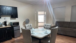 Een eethoek met een tafel voor vier personen, een keuken met donkere kastjes, een magnetron en een koffiezetapparaat.