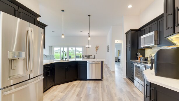 Una cocina moderna con armarios negros, electrodomésticos de acero inoxidable y piso de madera.