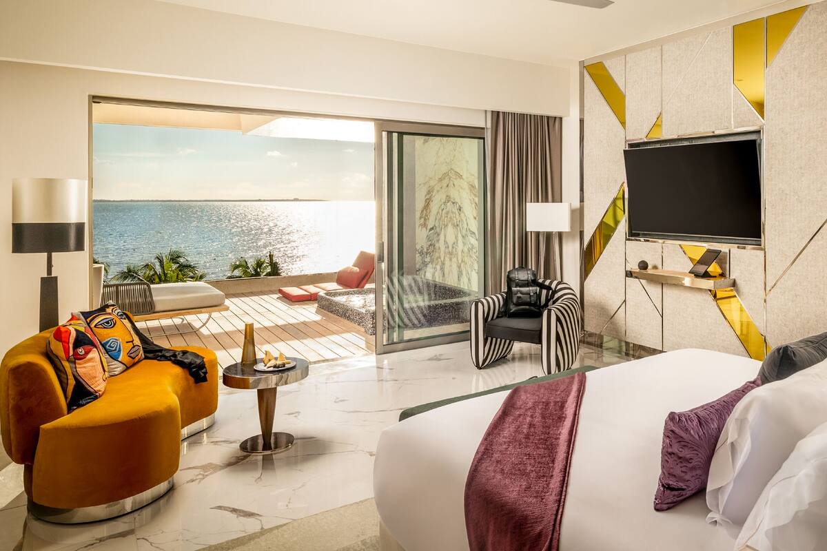 A hotel room with a large bed, a sofa, a TV, and a balcony with a view of the sea.