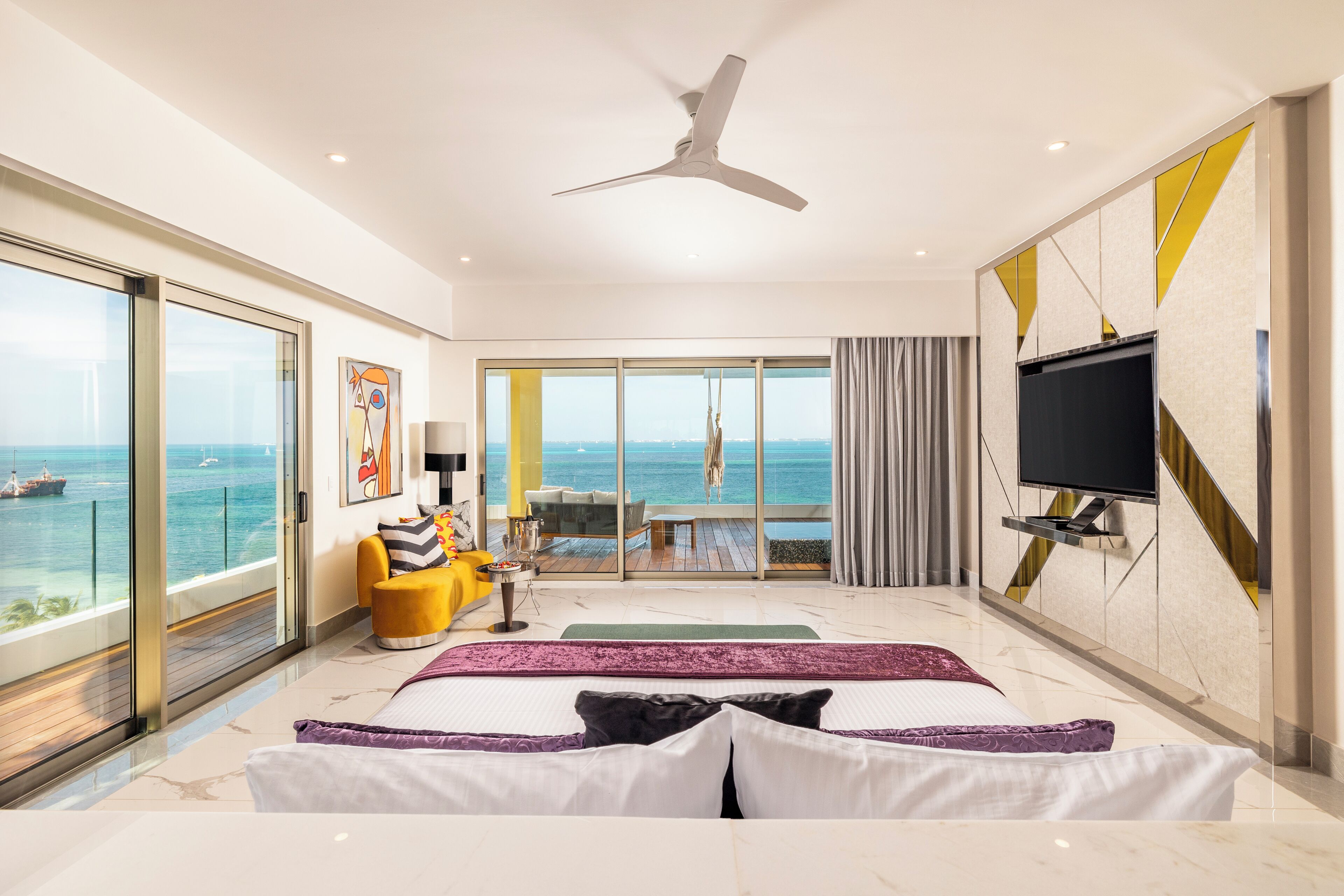 Una habitación de hotel moderna con una cama grande, televisión y balcón con vista al mar.