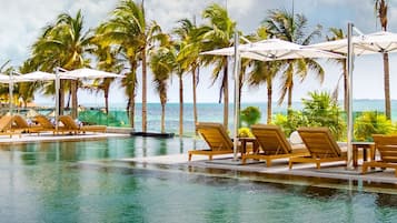 A pool area with lounge chairs and umbrellas, surrounded by palm trees and a view of the ocean.