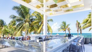 A bar area with a long counter, clear glasses, and a view of the ocean and palm trees. - Hotel Mousai Cancun Adults Only - All Inclusive (Punta Sam)