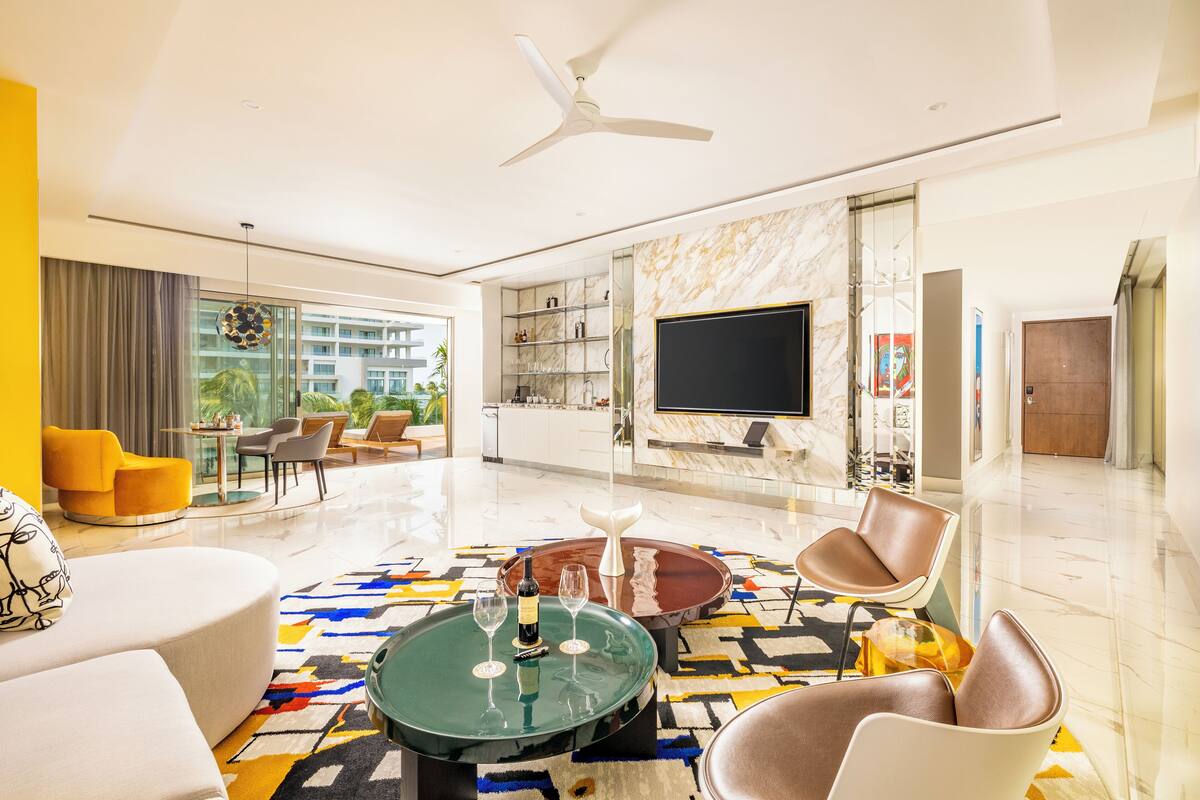 A modern living room with a large flat-screen TV, a ceiling fan, and a glass partition with shelves.