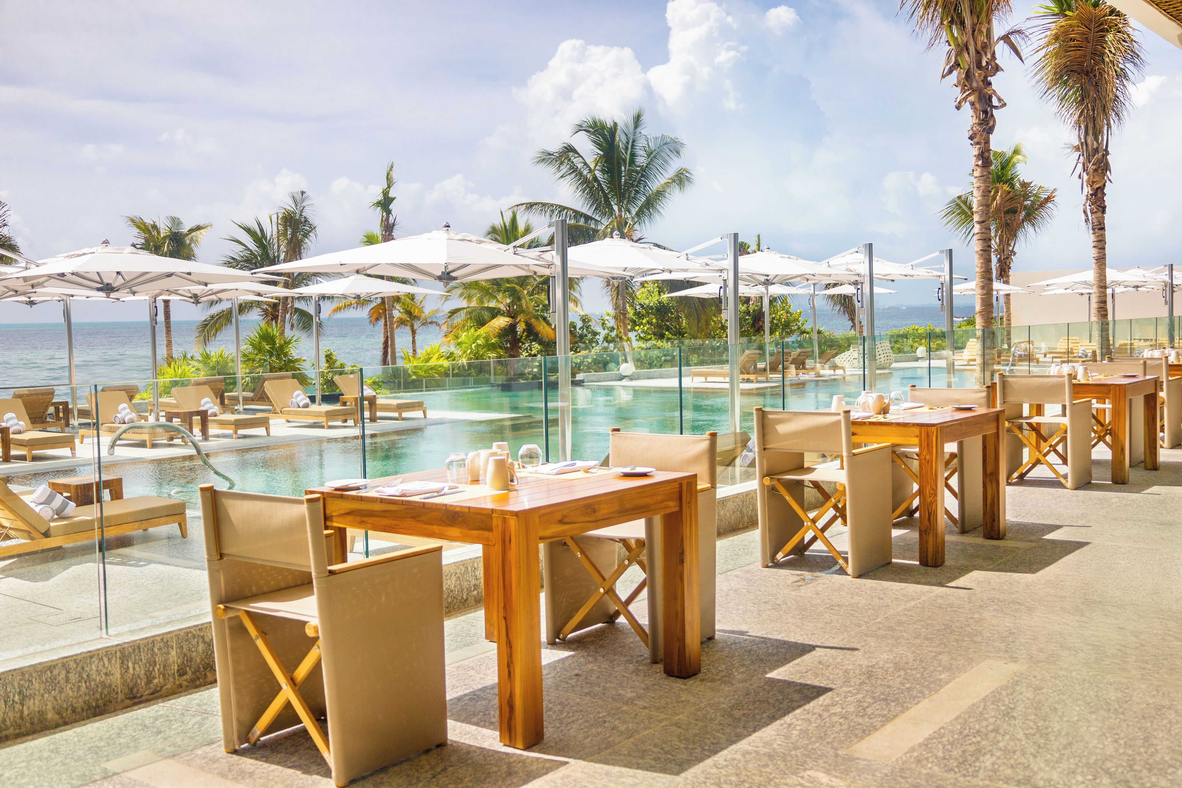 Zona de piscina con sillones de playa y sombrillas, con vistas al mar azul y transparente.