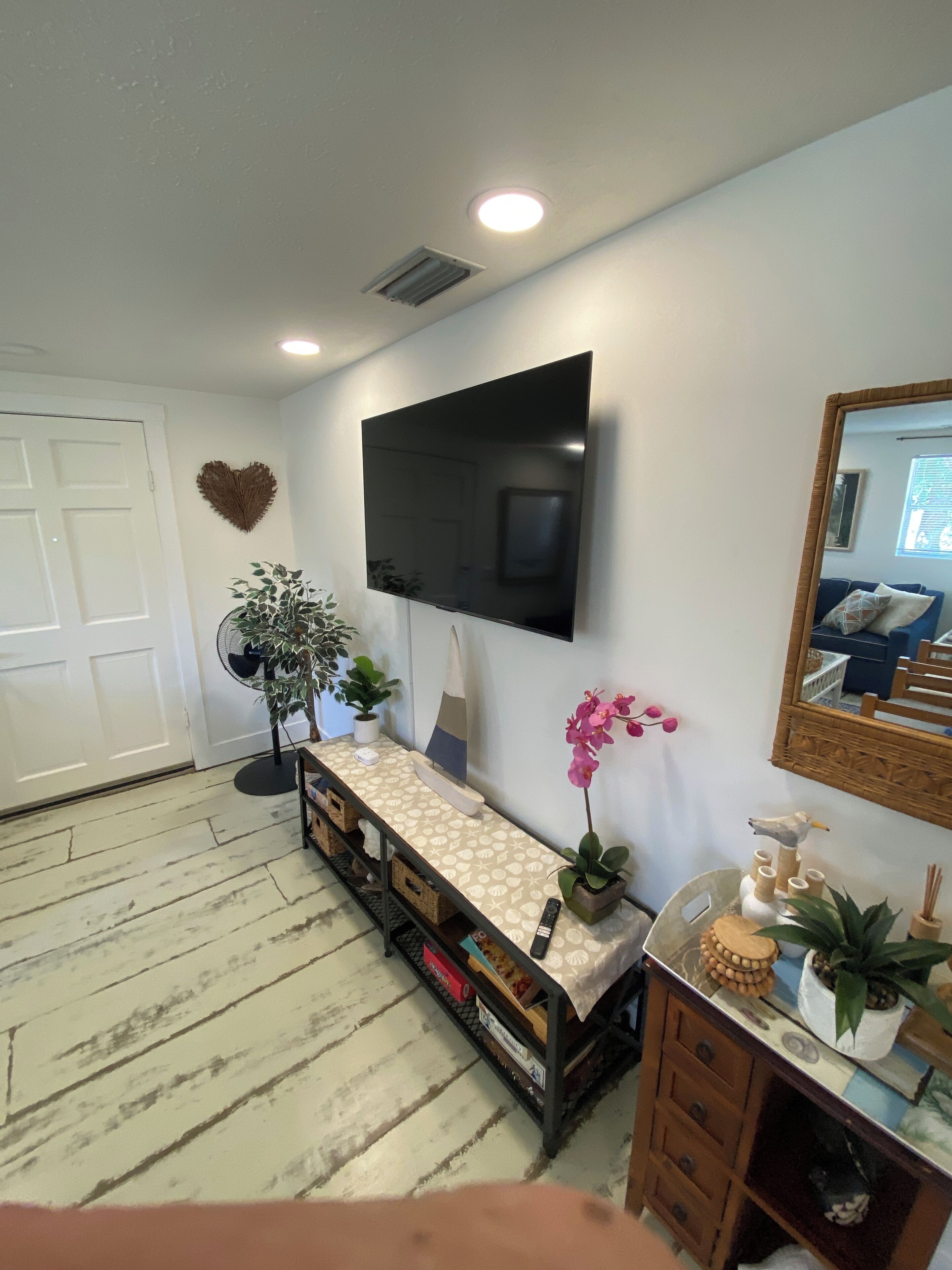 Ein Wohnzimmer mit Flachbildfernseher an der Wand, einer Bank mit Dekoration und einem Holzkasten mit Schubladen.