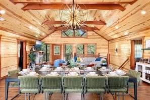 A wooden cabin interior with a dining area, a living room with a sofa and TV, and a kitchen area.