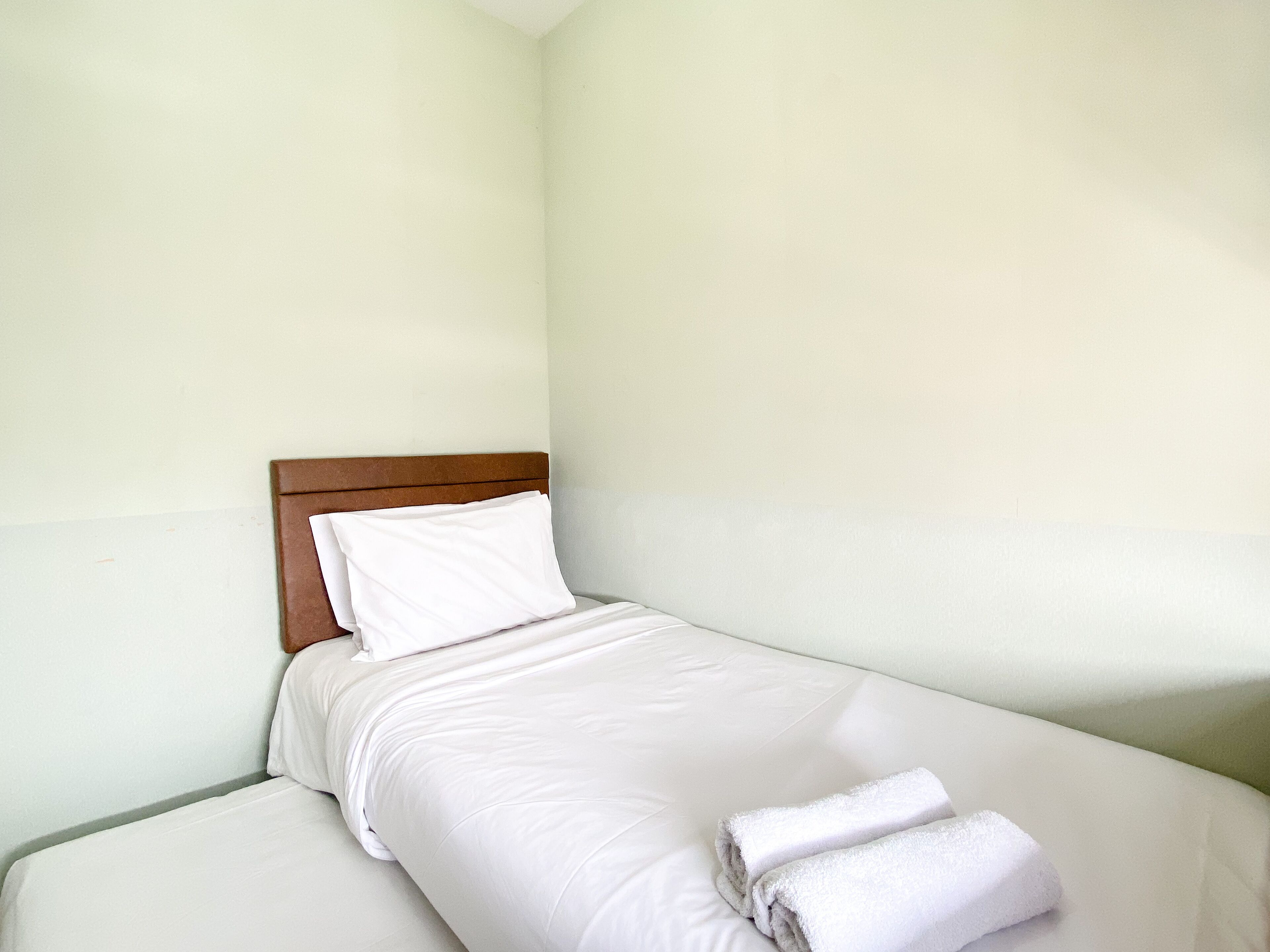 A single bed with white bedding and a wooden headboard in a room with plain walls.