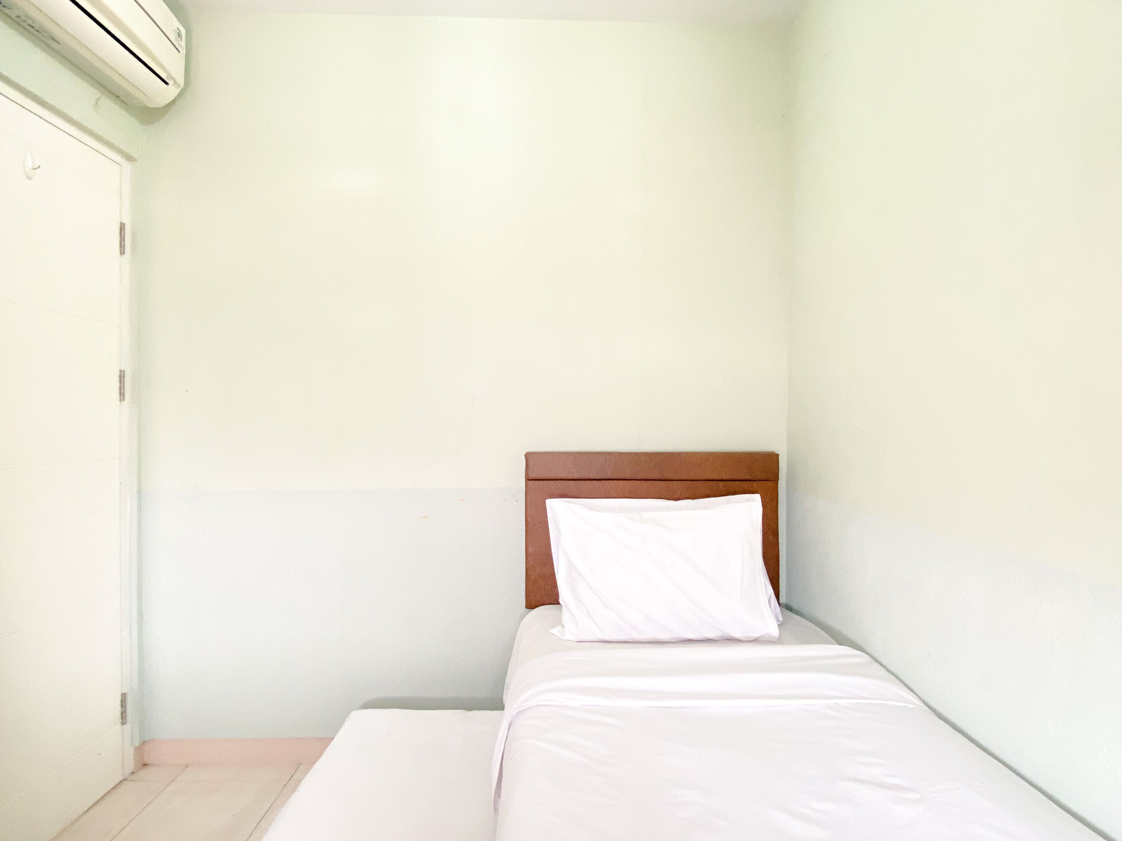 A small, single-bed room with a wooden headboard, white bedding, and a plain wall.