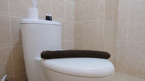 Een wit toilet met een bruine handdoek op de bril, een toiletrolhouder en een spuitfles voor een bidet.