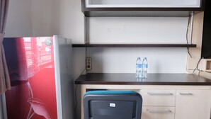 Een kleine keuken met een koelkast, een aanrecht met twee waterflessen en een stoel.
