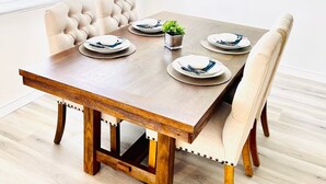 Ein Esszimmer mit Holztisch, gedecktem für vier Personen, gepolsterten Stühlen und einer Wanddekoration.
