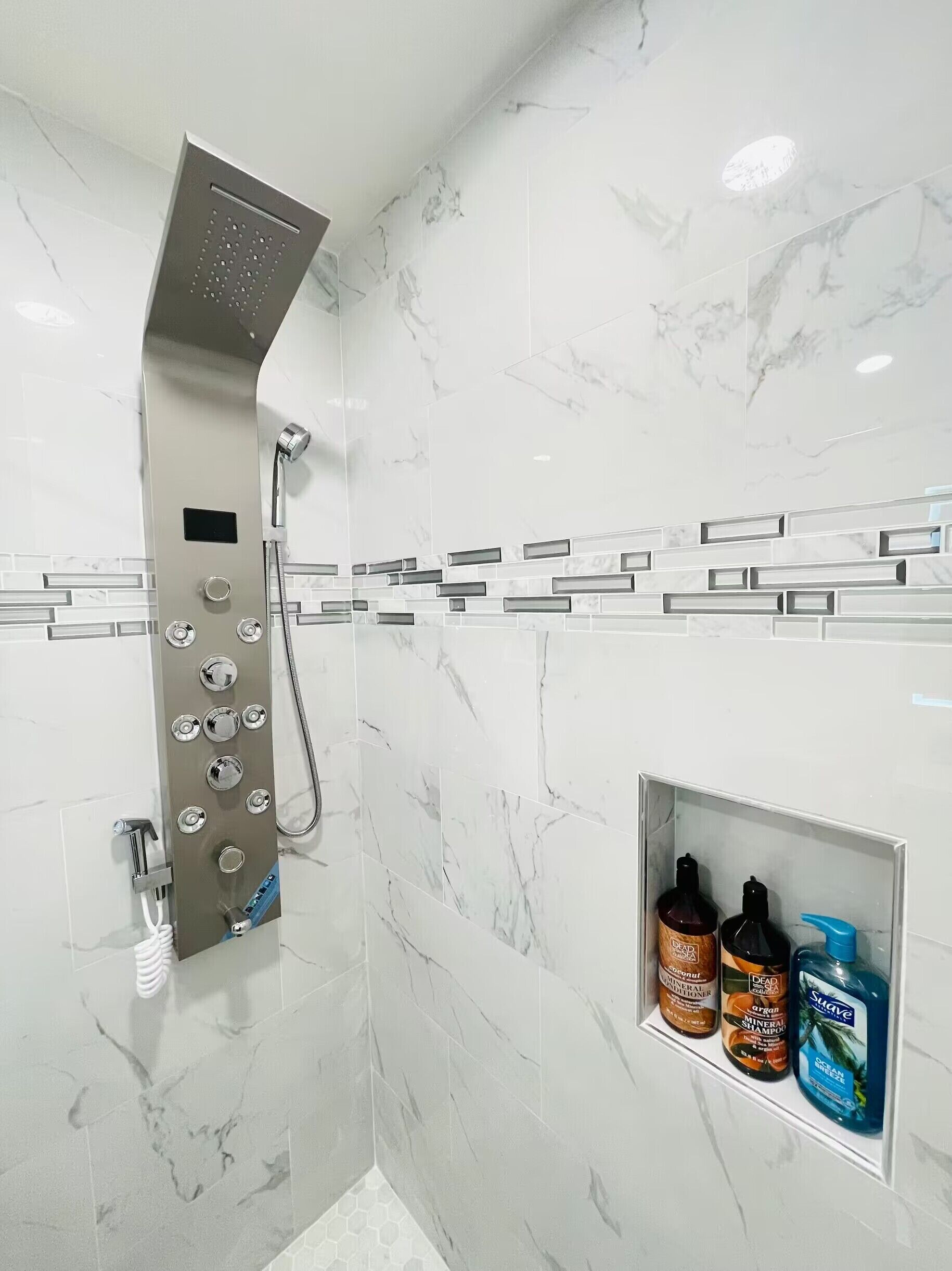 A bathroom with a shower, marble tiles, and a shelf with toiletries.