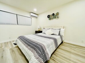 Une chambre à coucher comprenant un lit, une table de chevet, une lampe, un climatiseur mural et un élément décoratif fixé au mur.