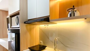 A modern kitchen with a built-in oven, a microwave, a black induction cooktop, and a stainless steel sink. - Comfort Stay Studio Room Pollux Chadstone Apartment (Cikarang)
