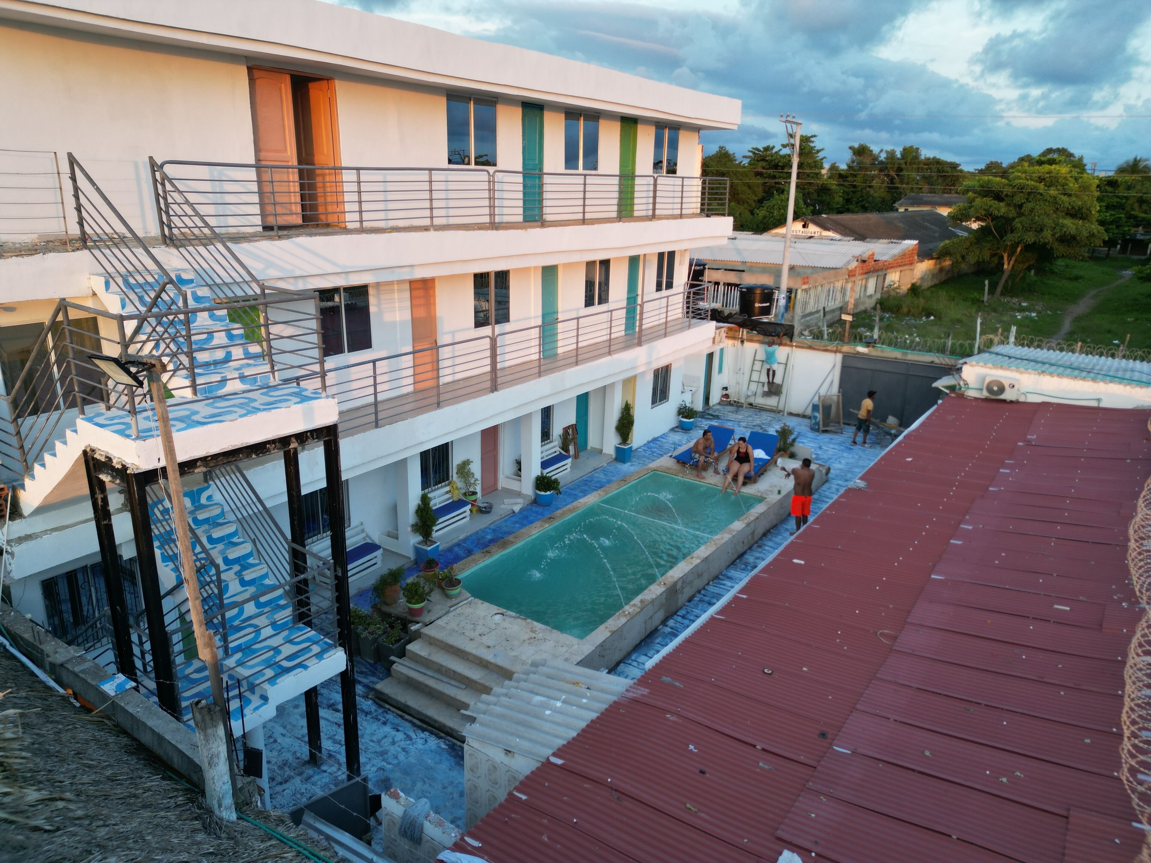 A multi-story building with a swimming pool, outdoor seating, and a red-roofed area.