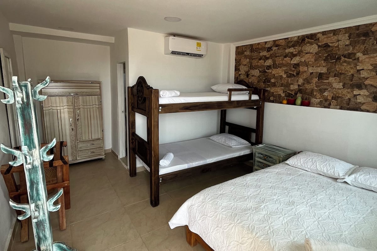 A room with bunk beds, a wardrobe, a desk, and a stone wall.