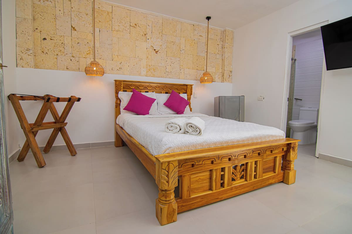 A wooden bed with a white mattress and two purple pillows, a wooden chair, and a wall with a textured pattern.